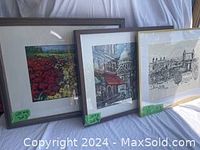 Three framed art prints standing side by side: floral print (left), Paris/London cityscape (middle), black and white cityscape (right).