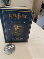 Front cover of Harry Potter Page to Screen collectors book showing blue cover with gold embossed text and Hogwarts image through star-shaped window.