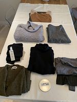 Photo of folded ladies designer sweaters and clothing items including sweaters, pants, and leggings all sized small, showing colors and fabric textures.