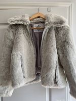 Front view of the light gray faux fur coat showing hood, zipper, and stuffed plush texture.