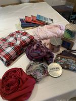 Photo showing red plaid pajamas, pink pajamas, three scarves, three small purses, three candles, and five assorted books.