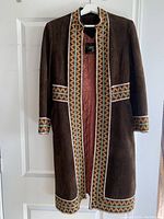 Front view of vintage dark brown suede coat with colorful beaded trim along front, cuffs, waist, and hem, hanging on hanger