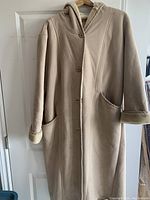 Front view of the XL beige faux suede and fur lined long coat hanging on a hanger, showing button closure and two front pockets.