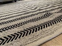Close-up angled photo showing woven texture and black chevron design on light grey cotton area rug.