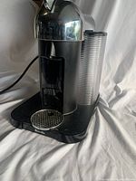 Front view of black and silver Breville Nespresso coffee maker showing dome top, drip tray, and ribbed water tank.