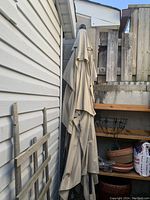 Beige outdoor sun umbrella folded closed and leaning against a wall, no base visible.