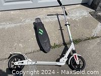 Full view of white Ride Volo scooter with green details and black Ten Toes penny board placed on ground