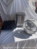 Silver tabletop fan, stainless steel step garbage bin, black Omcan induction stove on white background