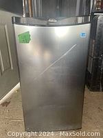 Full front view of the Sunbeam mini fridge showing stainless steel door with minor marks and tape residue.