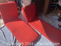 Two orange long lounge chair cushions placed on a surface. Both cushions appear thick and padded, designed for outdoor use.