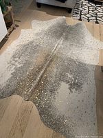 Full view of the vintage faux animal print rug on a wooden floor showing cream/beige base with black speckled pattern and gold accents mimicking an animal hide shape.