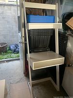 White particleboard ladder desk with shelves and cubby storage in a garage setting, showing angled frame, cubby space, and shelves