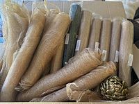 15 rolls of sinamay mesh ribbon, mostly gold color with one hunter green, and a gold glittered pinecone decoration, arranged on cardboard surface.