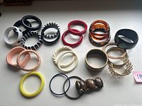 Overview of the 23 bangles and bracelets showing various colors, materials, and styles including black, brown, red, amber, cream, yellow, and gold-tone pieces.