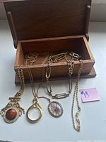 Photo of five gold-tone necklaces laid in and next to small wooden box, showing pendants and chain styles.