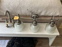 Bathroom faucet and lighting fixture set placed on a small white table, showing the brushed nickel finish and installation components.
