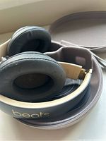 Close-up image of the Beats headphones folded inside the matching zippered carrying case, showing black ear cushions and gold headband.