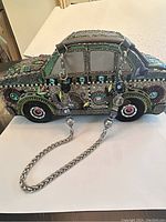 Side profile of the beaded car-shaped purse showing detailed beading, chain strap with decorative beads, and window embellishments.