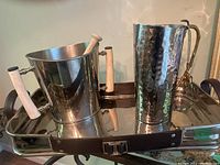 Wide view of metal tray holding ice bucket, hammered pitcher and ice tongs