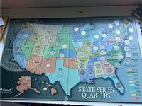 Front view of the HE Harris coin album showing a large US map with quarters placed in slots for various states, some states missing quarters, with states and years color-coded.