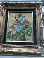 Full view of framed vintage oil painting depicting two blue birds on branches with pink flowers and green leaves, painted on tobacco leaves.