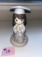 Front view of the brown-haired girl Precious Moments graduate figurine holding a diploma, standing on a round base decorated with pink roses.