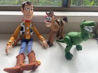Photo showing full set of three Toy Story figures: Woody, Bullseye, and Rex arranged near window.