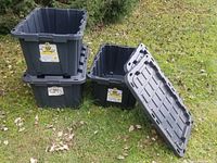 Three stacked and nested black plastic storage totes with one lid removed, showing interior and design.