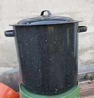 Full view of the blue enamelware canning pot with the lid on top, showing side handles and speckled blue finish.