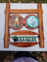 Front view of Philadelphia Eagles wooden wall clock showing two circular clocks (one with football player, one with Eagles logo) and a rectangular team name plaque.