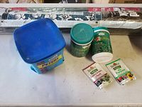 Containers of Peters plant food, Garden Basics fertilizer spikes, small packets of Burpee plant food, and roll of weed block fabric.