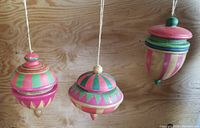 Three large painted wooden hanging ornaments in various colors and patterns photographed against wooden backdrop
