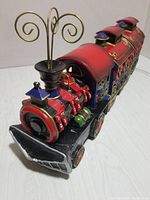 Front angled view of the red polyresin locomotive of the Christmas train with decorative gold accents and ornate chimney top.