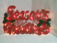 Lighted "Season's Greetings" sign with red lights and green holly leaf decorations, displayed unlit.
