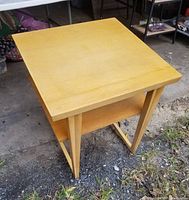 Full view of the square blond finish end table showing top and shelf with wear and minor stains.