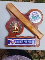 Front view of baseball bat shaped wall clock with Phillies logos, clock face with batter silhouette, and team name plaque.