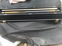 Pool cue disassembled inside the open hard case showing two pieces with wood grain design and black grip.