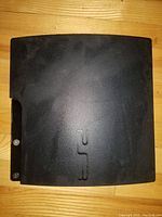 Top front view of PS3 console with visible PS3 embossed logo on black plastic casing, showing minor surface wear.