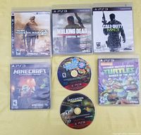 Photo shows seven PS3 games arranged on a flat surface: five in cases (Call of Duty Modern Warfare 2, The Walking Dead Survival Instinct, Call of Duty MW3, Minecraft PS3 Edition, Teenage Mutant Ninja Turtles Danger of the Ooze) and two discs only (LittleBigPlanet and Uncharted Drake's Fortune). ESRB ratings visible, cases show front covers.