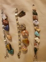 Photo depicting three vintage stone bracelets of various sizes and colors on linked chains, displaying natural polished stones attached individually.