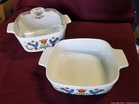 Two square Corning Ware casseroles and one glass lid, showing colorful Country Festival pattern. Lid placed on smaller casserole.