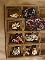 Top view of jewelry tray displaying multi-stone pin and five pairs of clip-on earrings with various designs and colors.