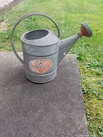 Full side view of the vintage galvanized watering can showing curved handle, spout with rose head and intact Wheeling label.