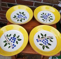 Four vintage Stangl Blueberry bowls with yellow rims and blueberry motif in the center.