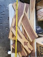 Multiple wood craft pieces stacked showing varying lengths, widths, wood grain and live edges, photographed with a tape measure about 12 inches long for scale.