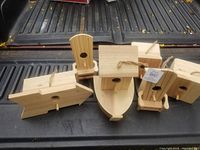 Top view of ten wooden birdhouses in various shapes including boat, armchair, small house, and others on a dark surface with some birdhouses tagged.