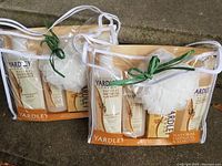 Two clear plastic bags each containing four Yardley Natural Oatmeal and Almond bath products and a white bath sponge tied with green string.