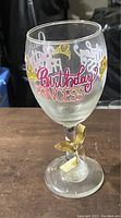 Front and side view of clear wine glass with Birthday Princess text and gold ribbon on stem