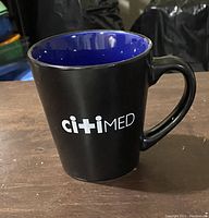 Side view of black mug with blue interior displaying white citimed logo