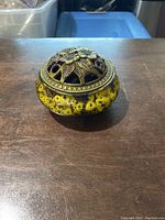 Incense holder placed on wooden surface showing side and angled view of lid and body